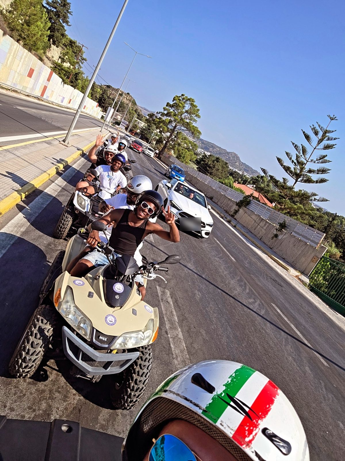 The team waving from a line of quad bikes on a sunny coastal road abroad